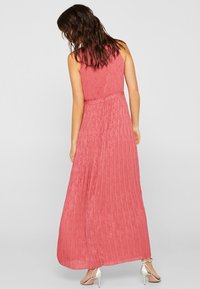 Dlouhé bezramínkové šaty v jemné korálové barvě s vertikálními sklady, přiléhavým živůtkem a splývavou sukní. Vyrobené z lehké látky.