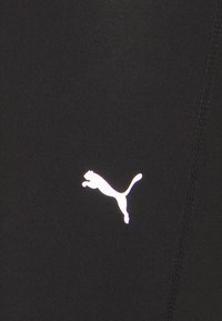 Czarne legginsy sportowe o gładkiej fakturze, z małym białym logo Pumy na dolnej części oraz szwami płaskimi.