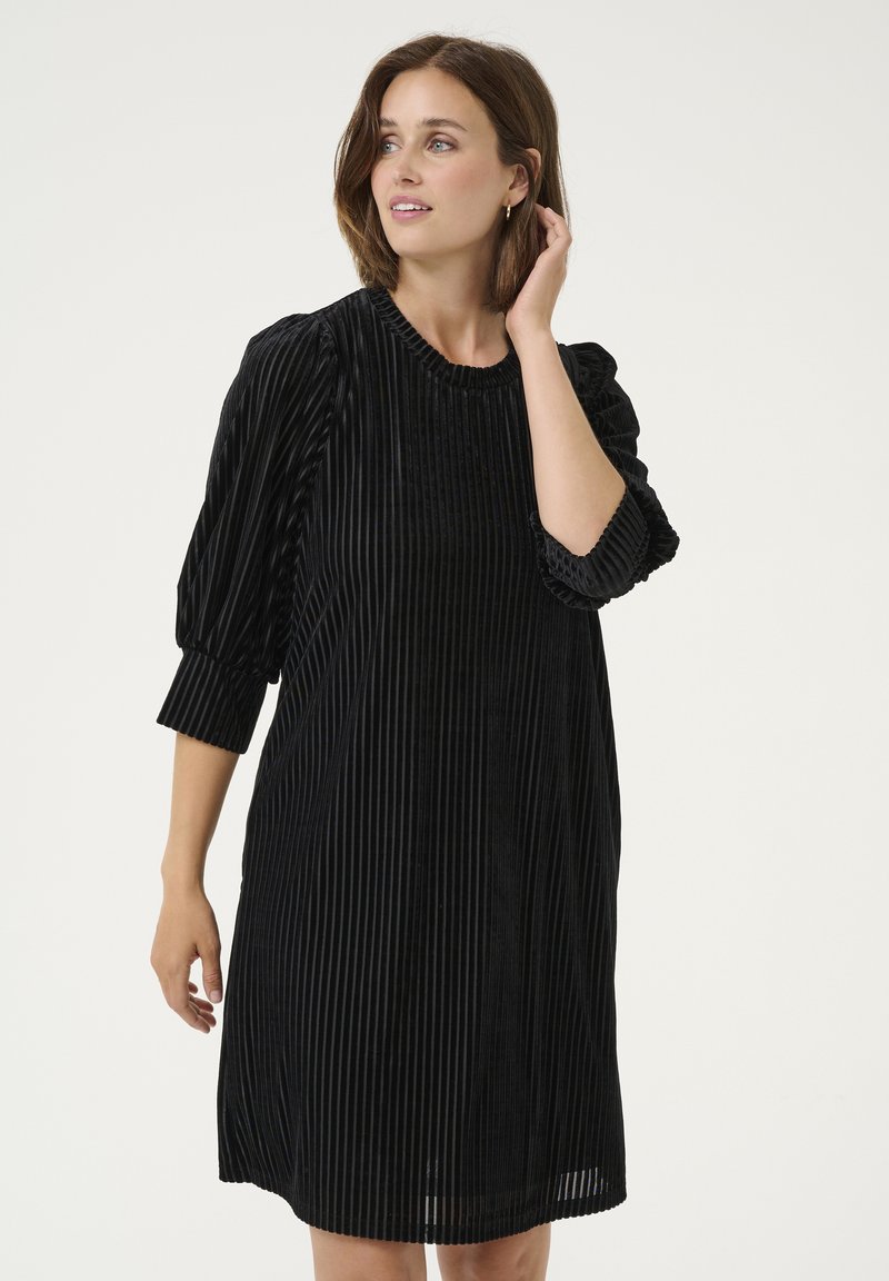 Vestido de pana negra con rayas verticales, escote redondo y mangas abullonadas. Corte midi con una textura suave, sin herrajes visibles.