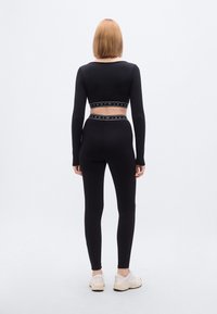 Μαύρο crop top με μακριά μανίκια και ψηλόμεσο κολάν με ελαστική ζώνη με λογότυπο, με εφαρμοστή σχεδίαση και λεία υφή.