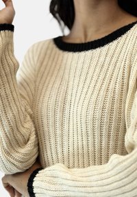Strickpullover in Creme mit schwarzem geripptem Kragen und Bündchen, der vertikale Streifen und Puffärmel für zusätzlichen Volumen bietet.