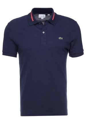 Granatowa koszulka polo z fakturowanej bawełny, z klasycznym kołnierzykiem w czerwono-białe paski, oraz zielonym logo Lacoste na piersi.