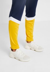 Sportiga joggers i marinblått och klar gult med vita detaljer, i kombination med vita mesh-sneakers med strukturerad överdel och elastiska remmar.