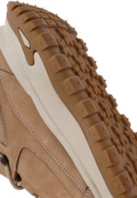 Zapatilla de gamuza marrón claro con una suela de goma que presenta patrones hexagonales texturizados. Acentos en beige claro en la media suela y detalles de costura.