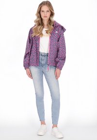 Fialová nepromokavá bunda s růžovým leopardím potiskem, elastické manžety, kapuce se stahovací šňůrkou, bílý tričko s grafikou, světle modré úzké džíny a bílé tenisky.