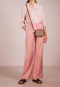 Chemise rose pâle boutonnée, pantalon large taille haute rose, et un sac bandoulière marron à motif. Des sandales slides noires texturées complètent le look.