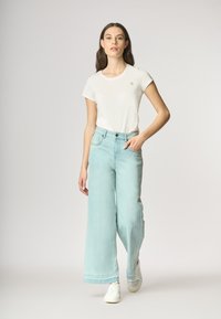 Jeans a gamba larga di un blu chiaro con vita alta, abbinati a una t-shirt bianca a maniche corte. Sneakers casual completano l'outfit.