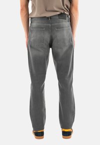 Vaqueros de denim gris con un corte recto, diseño de cinco bolsillos y costuras visibles. Llevados con zapatos oscuros que tienen acentos en naranja.