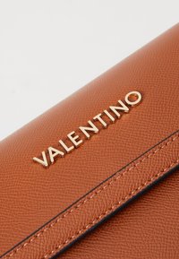 Brązowy portfel ze skóry o fakturze, z złotym logo „VALENTINO” oraz kontrastowym czarnym przeszyciem na krawędziach.