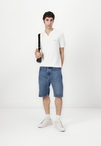 Vit kortärmad pikétröja med krage, tillsammans med blå denimshorts. Vita sneakers och en svart axelväska fulländar looken.
