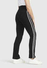 Schwarze Leggings mit hohem Bund, ausgestattet mit zwei vertikalen weißen Streifen an der Außenseite, aus dehnbarem Stoff gefertigt.