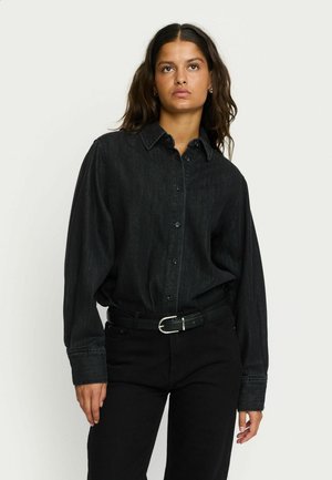 Black denim shirt with a button-up design, long sleeves, and a collar. Paired with black pants and a black belt featuring a silver buckle.