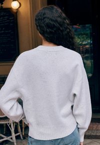 Light gray, textured sweater with dropped shoulders and ribbed hem. Paired with high-waisted blue jeans. Back view, showcasing soft fabric.