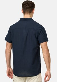 Camisa de manga corta color marino hecha de una tela ligera. Presenta un cuello de botón, dobladillo recto y un detalle de costura mínima.