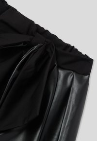 Gonna in pelle nera a vita alta con ampia fascia in tessuto e grande fiocco di stoffa annodato sul davanti.