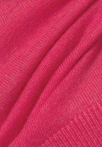 Heldere roze gebreide stof, met een gestructureerd patroon van zichtbare vezels, in zachte plooien gedrapeerd, met een gladde afwerking langs de randen.