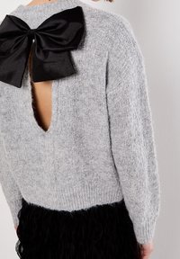 Pull gris duveteux avec un grand nœud noir dans le haut du dos et une grande ouverture en forme de trou de serrure révélant la peau en dessous.