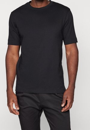 Schwarzes T-Shirt mit kurzen Ärmeln aus weicher Baumwolle. Verfügt über einen Rundhalsausschnitt und eine lockere Passform, kombiniert mit schwarzer Hose.