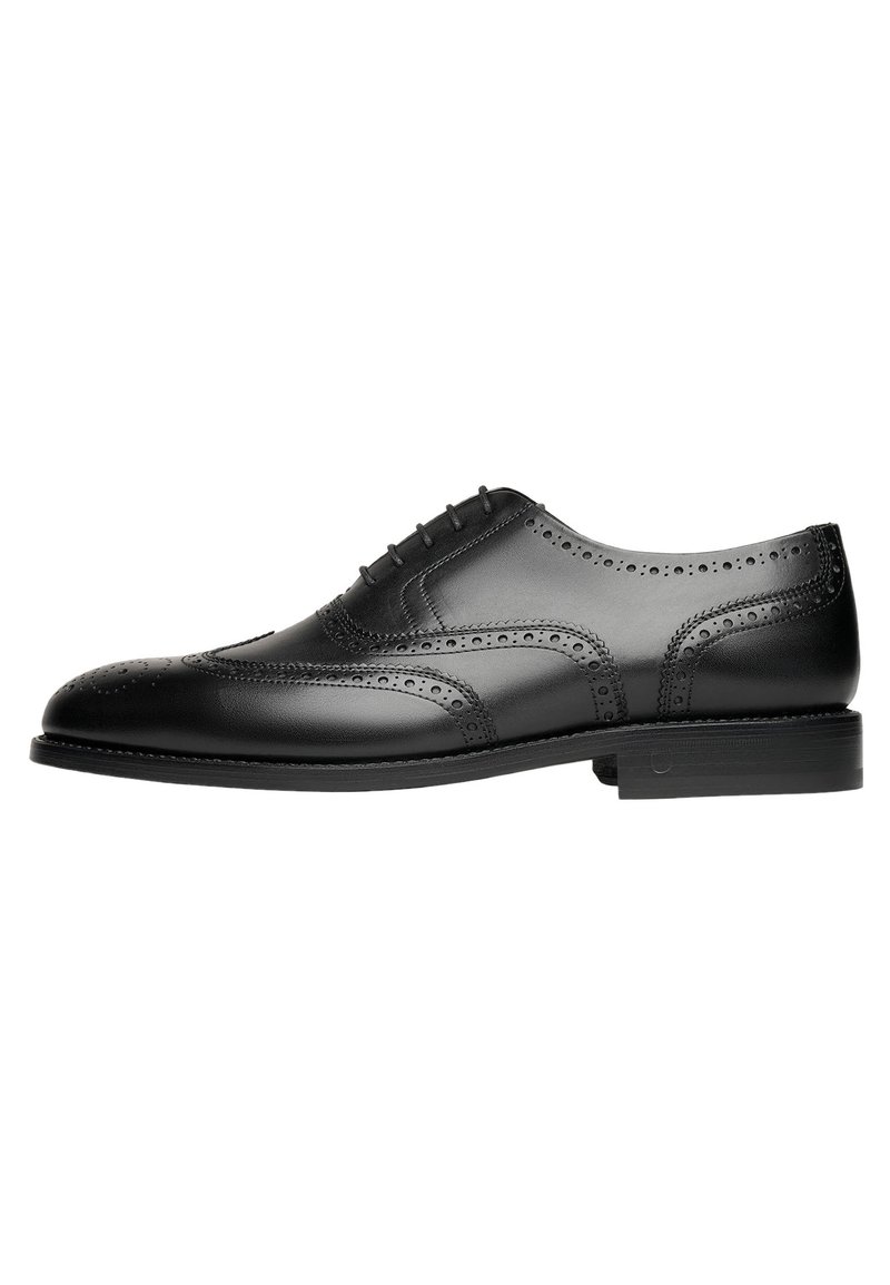 Scarpa da uomo in pelle nera con design wingtip, dettagli perforati e punta rotonda. Presenta una suola piatta con accenti di cucitura discreti.