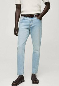 Jeans din denim de culoare albastru deschis, cu croi drept, asortați cu o curea din piele împletită de culoare maro și sandale de culoare maro închis, având o croială lejeră.