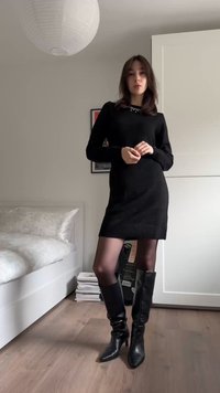 Mustast nöörkangast kleit soonikkoes äärega, kantud mustade läbipaistmatute sukkpükste ja põlvikutaolistel kontsakingadel. Taust on hele ning nähtaval on heledat värvi voodipesu.