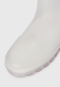 Botte en caoutchouc transparente avec un bout arrondi, semelle texturée et dessus lisse. Son design translucide offre une esthétique moderne et une résistance à l'eau.