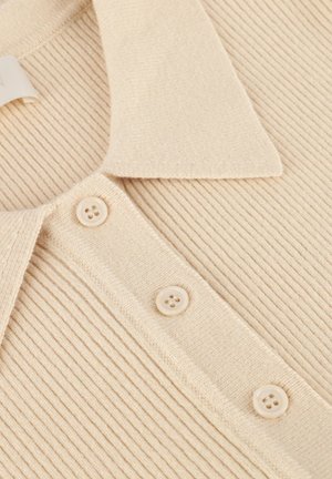 Close-up van beige ribgebreide stof met een kraag en drie bijpassende plastic knopen op een kledingstuk.