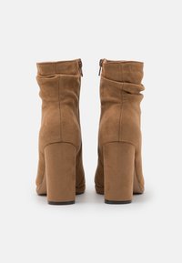 Bottes chevilles en daim marron avec un design froissé, talons carrés et fermetures éclair latérales, présentant une texture lisse et sans accents supplémentaires.