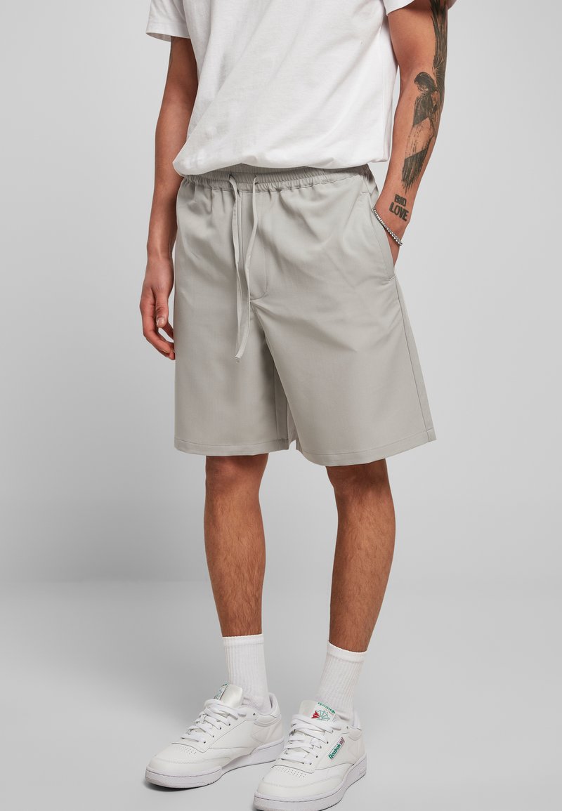 Pantalones cortos grises claros con cintura elástica y cordón, que cuentan con bolsillos laterales y un ajuste relajado, combinados con zapatillas blancas y calcetines.