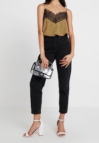 Gul leopardmönstrad linne med svarta spetsdetaljer, svarta högmidjade jeans, vita klacksandaler med blockklack och en genomskinlig handväska.