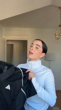 Black zippered jacket with white accents and Adidas logo; light, smooth fabric; model holds the garment against a neutral backdrop.