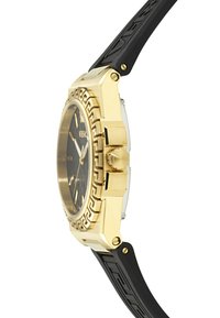 Reloj color dorado con una esfera negra con patrón, correa de caucho y caja octagonal. Sus características incluyen un borde texturizado y una corona prominente.