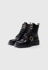 Black leather ankle boots with a rounded toe, metallic studs, side zipper, lace-up front, and a buckle detail. Thick textured sole.