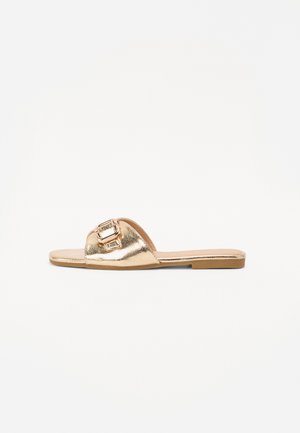 Gouden metalen slippersandal met een brede band, voorzien van een vierkante gespaccent, platte zool en een gladde textuur.