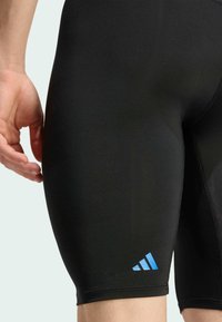 Crne sportske kratke hlače od rastezljivog materijala, s plavim Adidas logotipom na donjoj strani. Glatka tekstura i prilagođen dizajn.