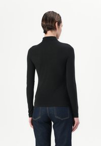 Czarny longsleeve z golfem, wykonany z miękkiego materiału, dopasowany fason i gładka faktura. Noszony z ciemnymi dżinsami, widok z tyłu.