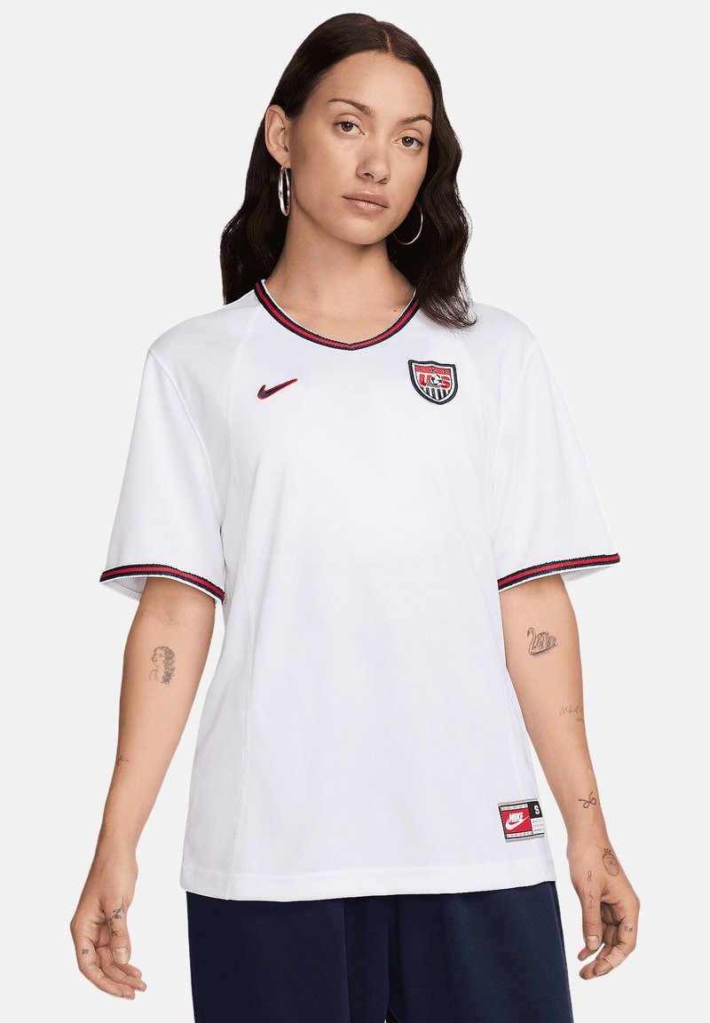 Maglia bianca Nike a maniche corte, con scollo a V e bordi rossi/blu. Presenta il logo della U.S. Soccer sul petto e l'etichetta del marchio sull'orlo. Tessuto morbido.