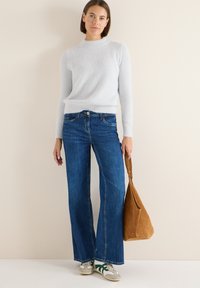 Jasnoniebieski sweter o fakturze, rozszerzane ciemnoniebieskie dżinsy, beżowa torba i sneakersy z zielonymi akcentami. Prosty design w neutralnych kolorach i casualowy styl.