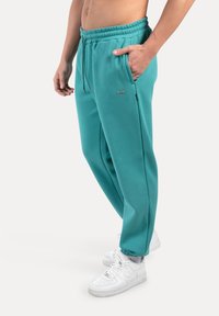 Teal sweatpants met een elastische tailleband, zijzakken en een klein logoaccent. Gladde stof met een ontspannen pasvorm. Gemaakt in combinatie met witte sneakers.