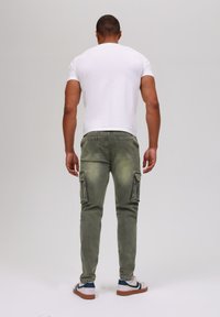 Men's white short-sleeve t-shirt, green cargo pants with side pockets, and white sneakers with navy accents. Simple, casual outfit from the back.