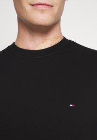 T-shirt in cotone nero con collo a girocollo, caratterizzato da un piccolo logo tricolore sul lato sinistro del petto. Il tessuto è liscio con una forma aderente.
