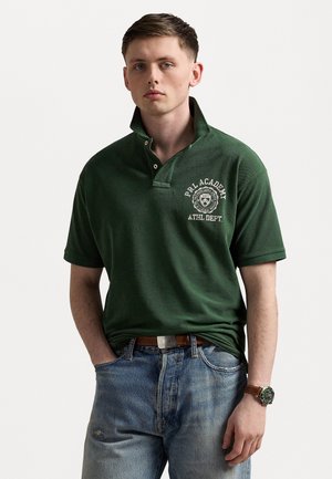 Donkergroene polo-shirt met een kraag met knopen en het geborduurde logo "PRL ACADEMY". Draag het met lichtblauwe jeans en een bruine riem.
