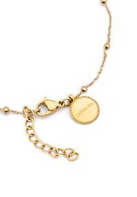 Pulsera de cadena de oro con cuentas esféricas, cierre de langosta y una etiqueta redonda grabada con "SINGULARU". Textura suave con acabado brillante.