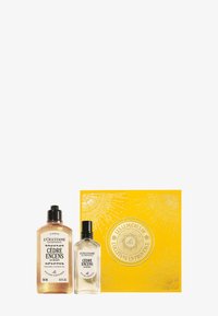 Zestaw upominkowy Cèdre Encens zawierający matową szklaną butelkę perfum oraz przezroczysty żel pod prysznic w ozdobnym żółtym pudełku z wytłaczanymi wzorami.