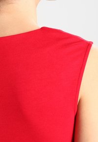 Haut sans manches rouge avec une texture lisse et un col rond, présentant des coutures nettes et un design minimaliste.