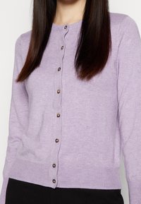 Cardigan lilas en tissu doux, avec un col rond, des manches longues et une fermeture boutonnée avec des boutons foncés. Texture lisse.