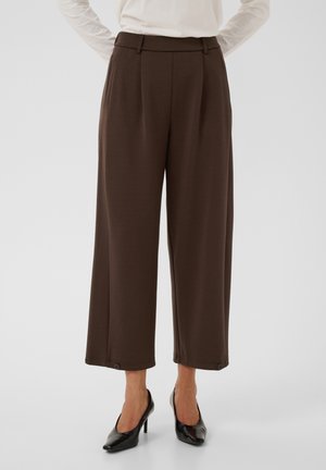 Pantalon marron large et court, porté avec des talons noirs, visible de la taille aux chevilles sur un fond uni.