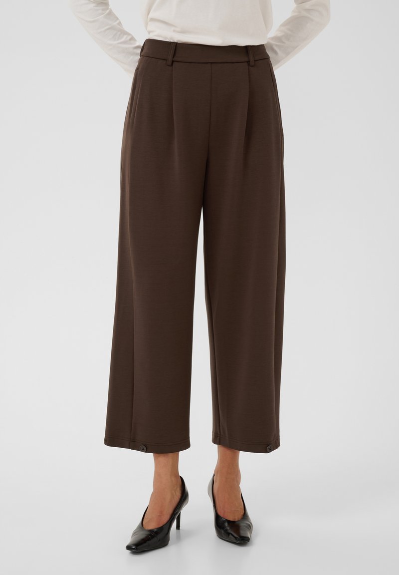 Pantalon marron large et court, porté avec des talons noirs, visible de la taille aux chevilles sur un fond uni.