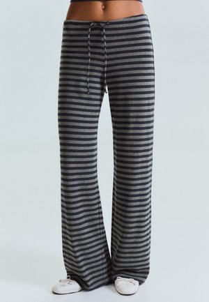 Personne portant un pantalon ample à rayures horizontales gris foncé et clair, avec une taille avec cordon et des chaussures blanches faciles à enfiler.