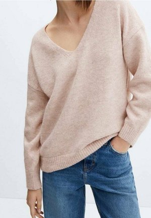 Vaaleanpunainen, väljä neulepusero syvällä V-pääntiellä, ribbireunuksilla hihoissa ja helmassa. Yhdistetty sinisiin farkkuihin, mikä korostaa rentoa tyyliä.